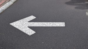 Flèche blanche peinte sur une route en asphalte pointant vers la gauche – Signalisation et orientation