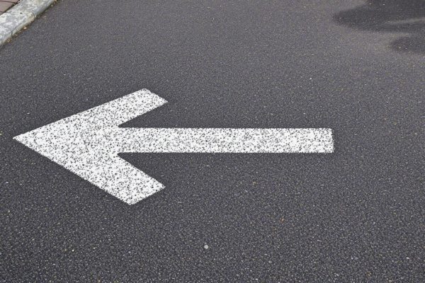 Flèche blanche peinte sur une route en asphalte pointant vers la gauche – Signalisation et orientation